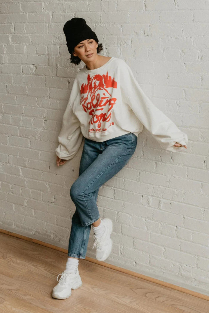 A woman in a white Rolling Stones NYC sweatshirt and jeans looking relaxed and stylish. People of Leisure Sweatshirt