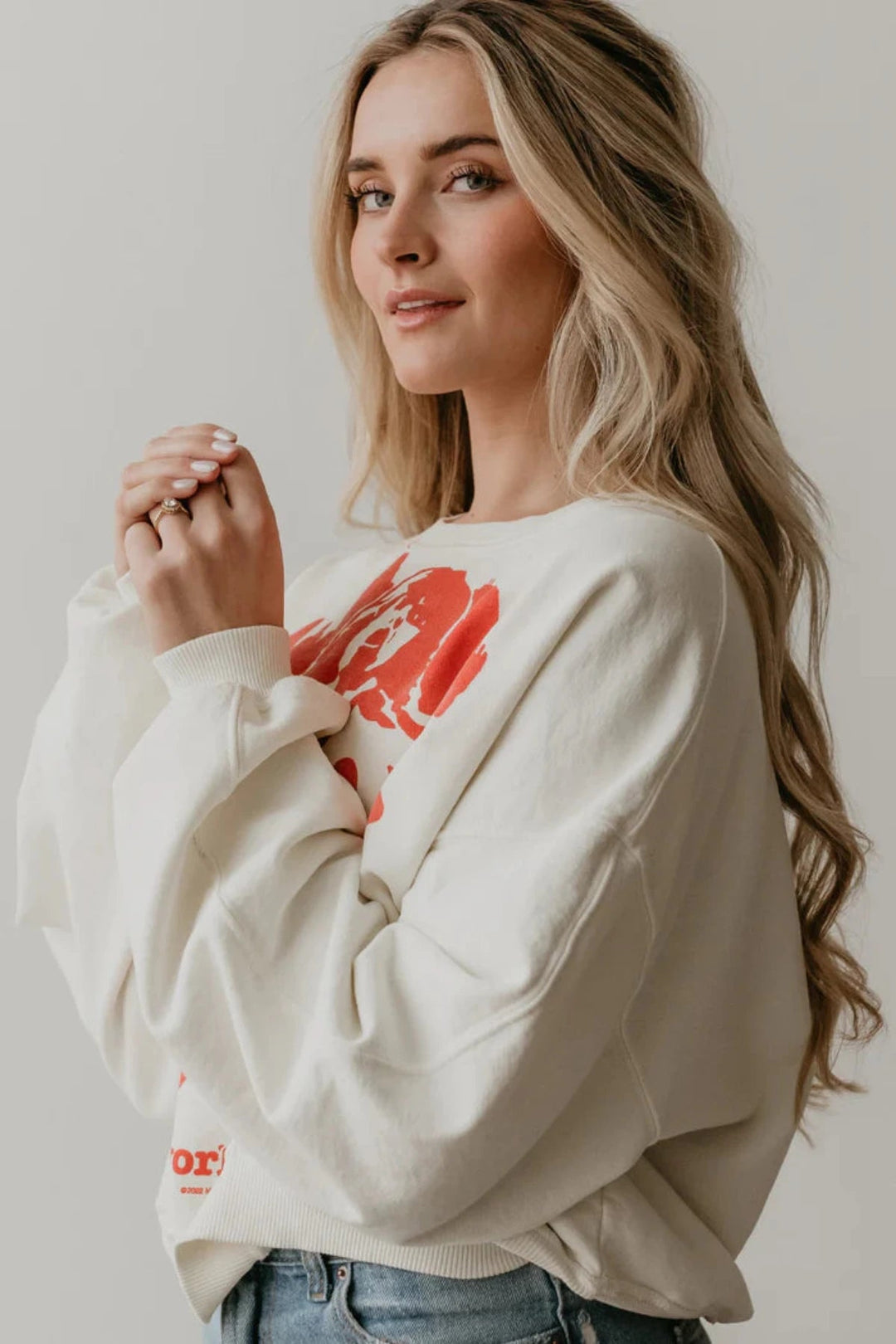 A woman in a white Rolling Stones NYC sweatshirt and jeans looking relaxed and stylish. People of Leisure Sweatshirt